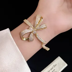 Elegant gold-tone bow bracelet encrusted with glittering zircons shown on wrist detail.