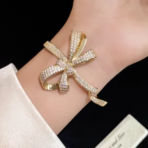 Detailed view of a gold bow bracelet inlaid with shimmering zircons on a wrist.