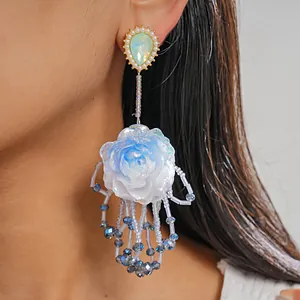 Close-up detail of blue resin flower earring with pearl and tassel accents on model
