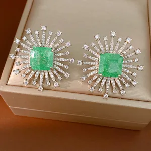 Dettaglio di orecchini a raggiera con pietra centrale verde e accenti di pavé.