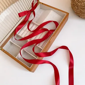 Close-up of long red satin ribbon hair accessory presented in a wooden jewelry box.