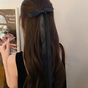 Close-up detail of a elegant black long ribbon bow hair clip on long brown wavy hair