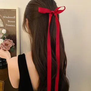 Detail of a red satin bow hair clip with long ribbons on brown hair, ballet style