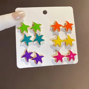 Juego de 12 pendientes de estrella coloridos con bordes dorados en tarjeta blanca.