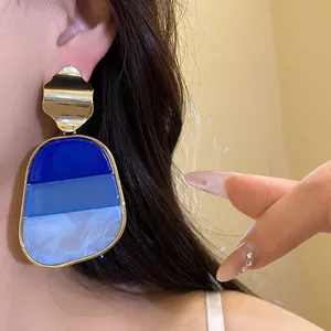 Primer plano de pendientes vintage con degradado azul y tachuelas metálicas doradas.