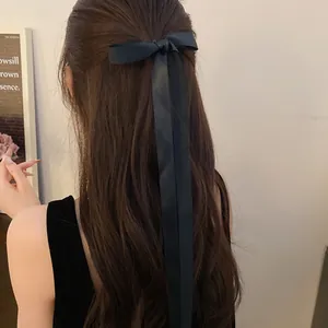 Detailed view of an elegant long black satin ribbon bow hair clip styled on long wavy hair.