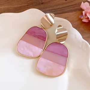 Detalle de pendientes colgantes de resina jaspeada rosa con elegantes cierres ondulados