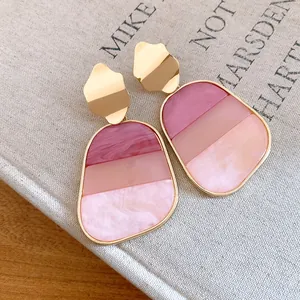 Detalle de pendientes colgantes retro de resina rosa con bloques de color y marco de metal dorado