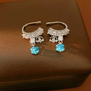 Close-up of silver fleur-de-lis ear cuffs with zircon and blue crystal cube charms