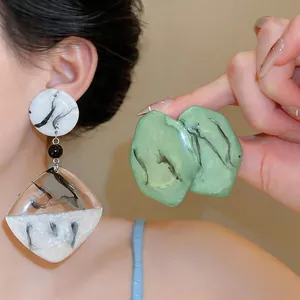 Détail de boucles d'oreilles en résine marbrée aux formes géométriques et organiques