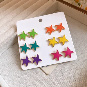 Detalle de un juego de 12 pendientes de estrella de colores en tarjeta blanca.