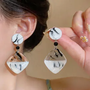 Gros plan de boucles d'oreilles géométriques en résine de style lavis d'encre chinois.