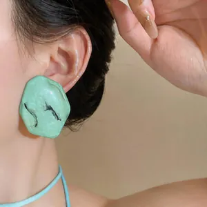 Gros plan sur des boucles d'oreilles en résine vert menthe au design géométrique irrégulier.