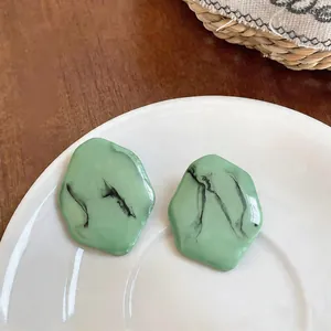 Vue détaillée des boucles d'oreilles en résine marbrée verte sur une assiette blanche.