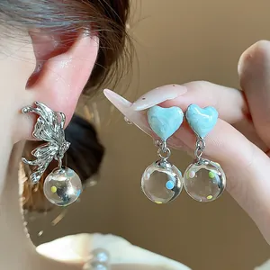 Close-up of heart-shaped blue enamel and butterfly silver earrings with glass ball