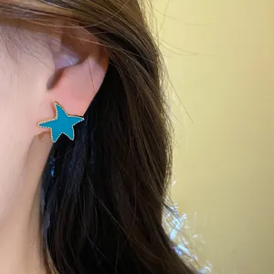 Pendiente de estrella turquesa con borde dorado mostrado en la oreja de una modelo