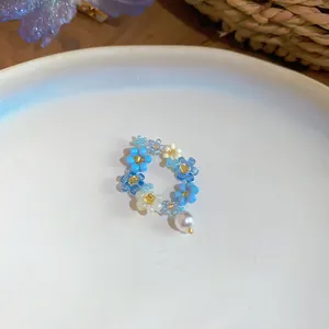 Gros plan d'une bague fleur en perles bleues faite main avec un pendentif perle blanche