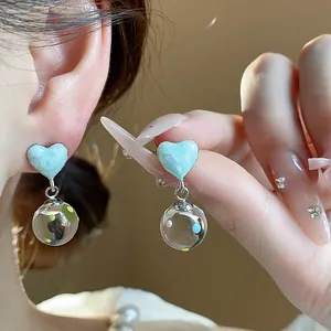 Close-up detail of heart-shaped light blue oil-drip earrings with clear glass ball drops