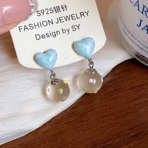 Close-up of light blue heart stud earrings with colorful polka dot glass ball dangles.