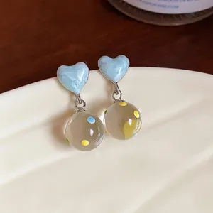 Close-up detail of light blue heart stud earrings with colorful dotted glass pendants.