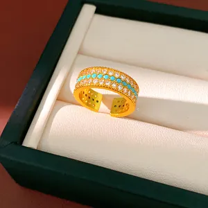 Dettaglio di un anello dorato con tre file di zirconi bianchi e perline color turchese