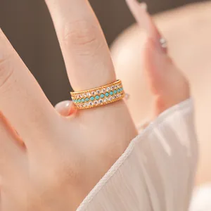 Primo piano di un anello dorato a tre file con zirconi bianchi e pietre turchesi sul dito
