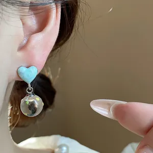 Close-up of elegant light blue heart-shaped earring with polka dot glass ball pendant on model