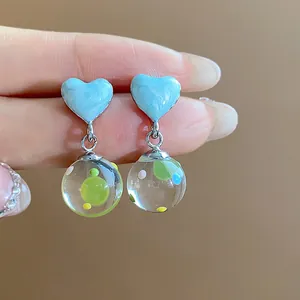 Close-up of blue heart drip oil earrings with colorful glass ball pendants.