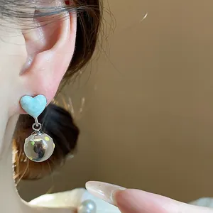Close-up view of light blue enamel heart earrings with a dangling speckled glass ball