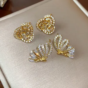 Macro view showing detailed zircon pavé on gold butterfly and clover stud earrings