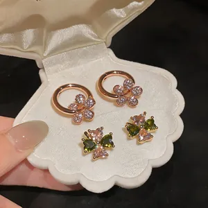 Detailed view of rose gold flower hoop earrings and colorful clover studs in shell box