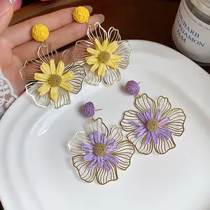 Dettaglio di orecchini a fiore in metallo traforato con centri in raffia gialla e viola