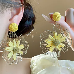 Vista dettagliata degli orecchini a fiore in rafia gialla con petali dorati traforati