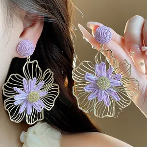 Dettaglio macro di eleganti orecchini a fiore in rafia viola con petali in metallo oro.