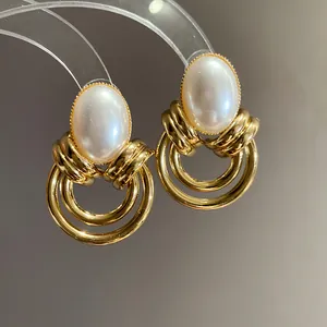 Dettaglio macro di orecchini vintage dorati con grandi perle ovali e tripli cerchi