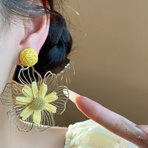 Vista dettagliata di orecchini a perno a fiore in raffia gialla e metallo su modella