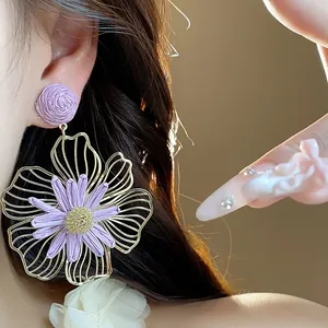 Dettaglio di orecchini a fiore in rafia viola con design in filo d'oro su modella