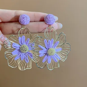 Dettaglio di orecchini pendenti in metallo dorato e rafia viola a fiore.