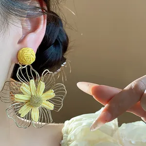 Primo piano di un grande orecchino a fiore in raffia gialla con cornice metallica