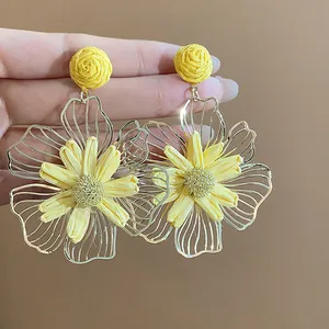Dettaglio ravvicinato di orecchini a fiore in rafia gialla con petali dorati traforati