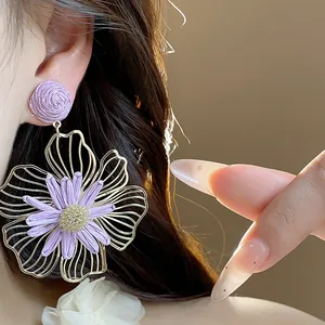 Primo piano dell'orecchino a fiore in rafia viola con petali dorati traforati.