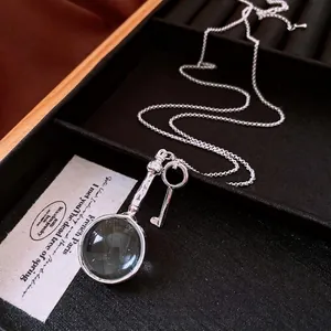 Collana vintage in argento con ciondoli lente e chiave su un display nero