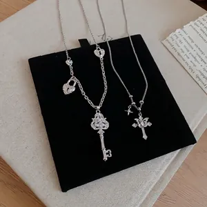 Ensemble collier clé et croix en zircon argenté présenté sur fond de velours noir