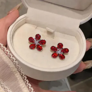Close-up of elegant silver flower stud earrings with red zircon petals in a gift box
