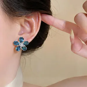 Close-up of elegant flower stud earring with blue zircons on an Asian model's ear.
