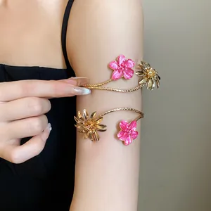 Detailansicht eines eleganten goldenen Metall-Armrings mit rosa Emaille-Blumen am Oberarm