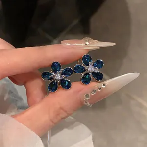 Macro view of blue flower stud earrings featuring sparkling zircon crystals held by hand