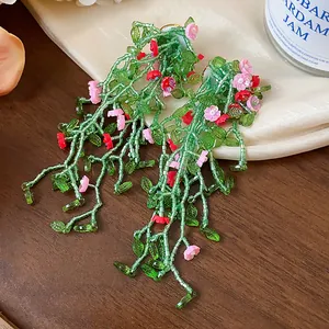 Macro view of handmade forest style green glass beaded tassel earrings with pink flowers
