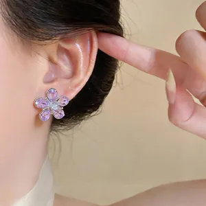 Macro detail view of sweet purple flower-shaped zircon stud earrings worn on a model's ear