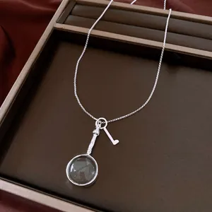 Dettaglio di una collana vintage con ciondolo lente e chiave argento su vassoio marrone